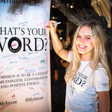 A girl smiling and writing down her word on a board while wearing her MyIntent white t-shirt