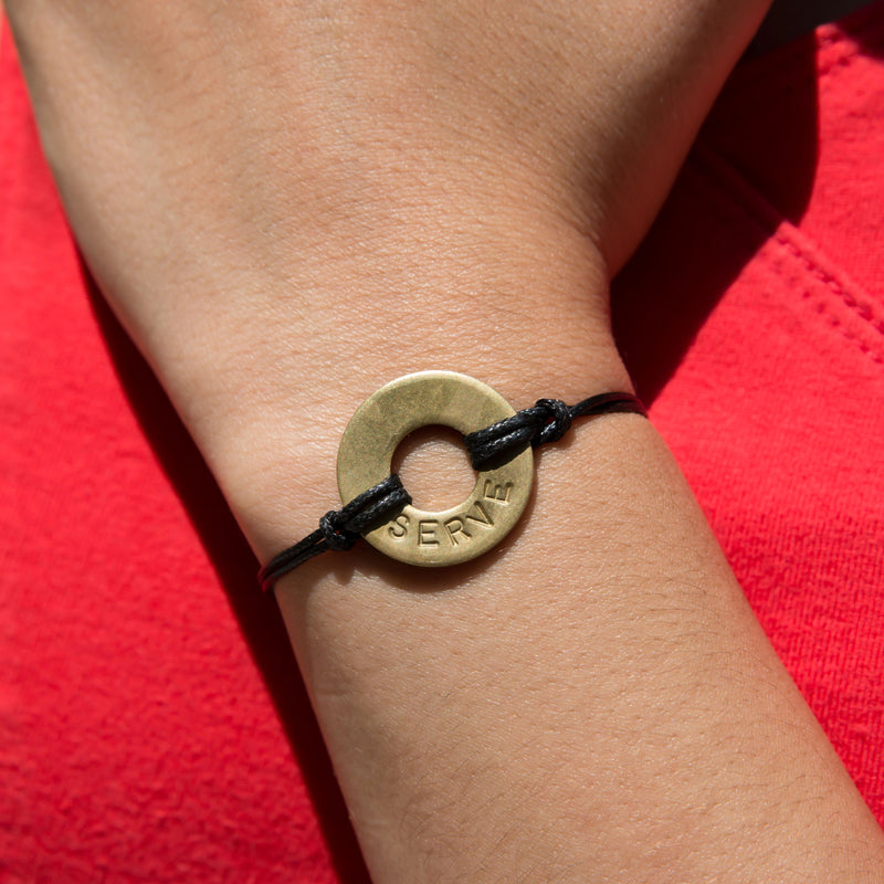 Girl wearing her MyIntent Custom Classic Bracelet Antique Brass Token Black String with word SERVE