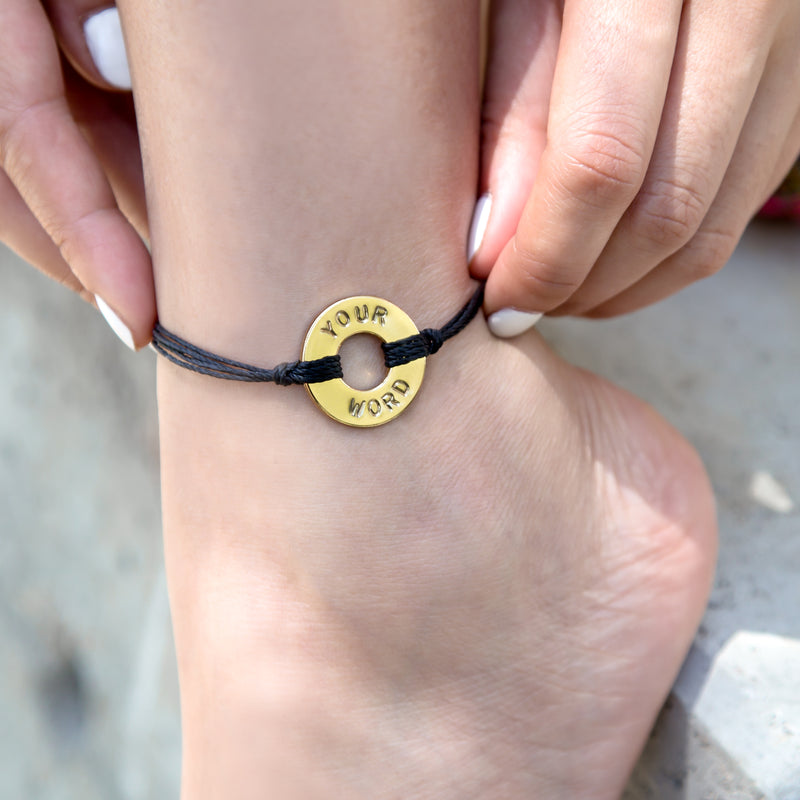 A girl adjusting her MyIntent Custom Twist Anklet Black String with Gold Token 