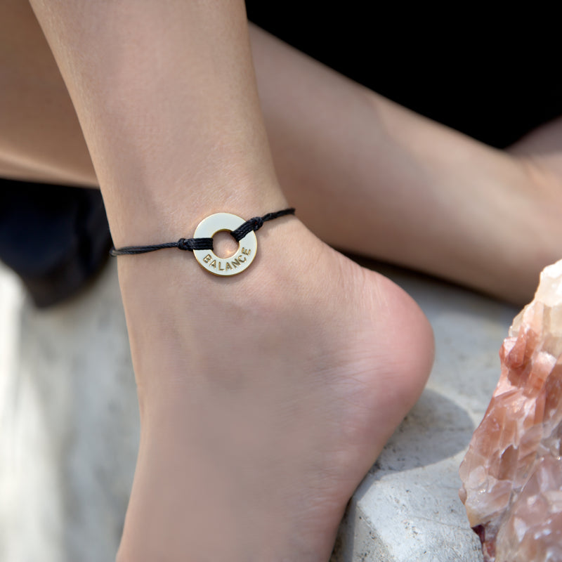 A girl wearing her MyIntent Custom Twist Anklet Black String Gold Token with the word BALANCE