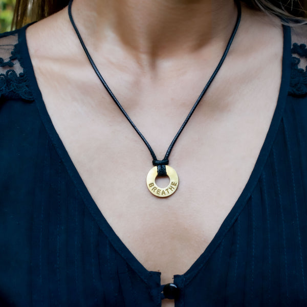 A girl wearing her MyIntent Custom Adjustable Black Necklace with Brass Token with the word BREATHE