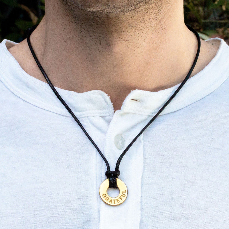 A guy wearing his MyIntent Refill Adjustable Black Necklace with Gold Token with the word GRATEFUL