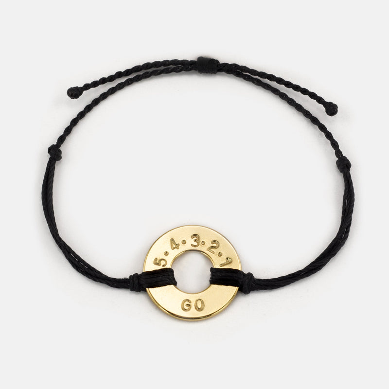 Mel Robbins' signature Twist Bracelet Black String Gold Token with the message 5.4.3.2.1.GO!