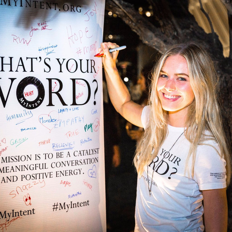 A girl smiling and writing down her word on a board while wearing her MyIntent white t-shirt
